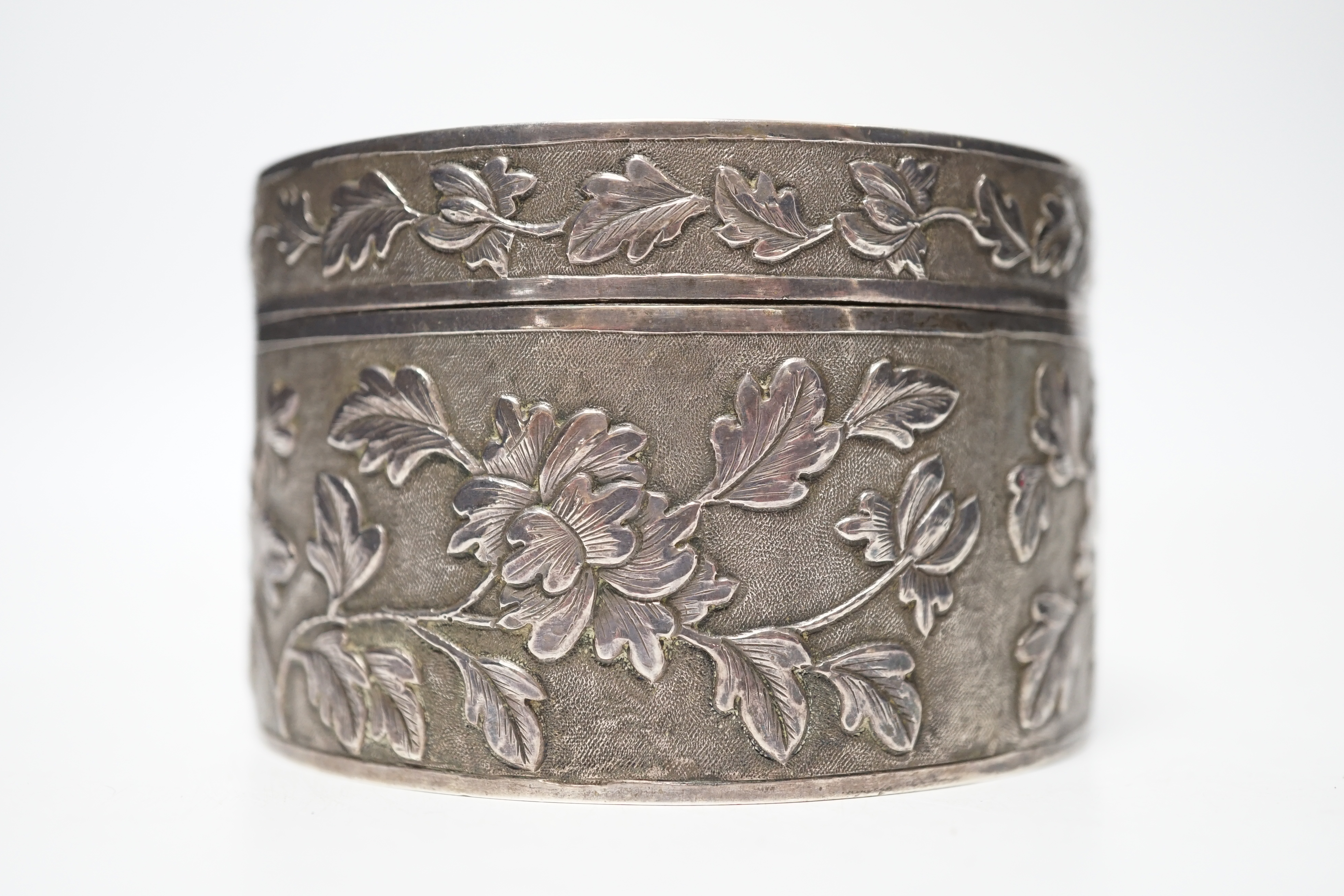 An early 20th century Chinese white metal circular box and cover, maker's mark MK, with foliate decoration and engraved inscription, diameter 82mm, 128 grams.